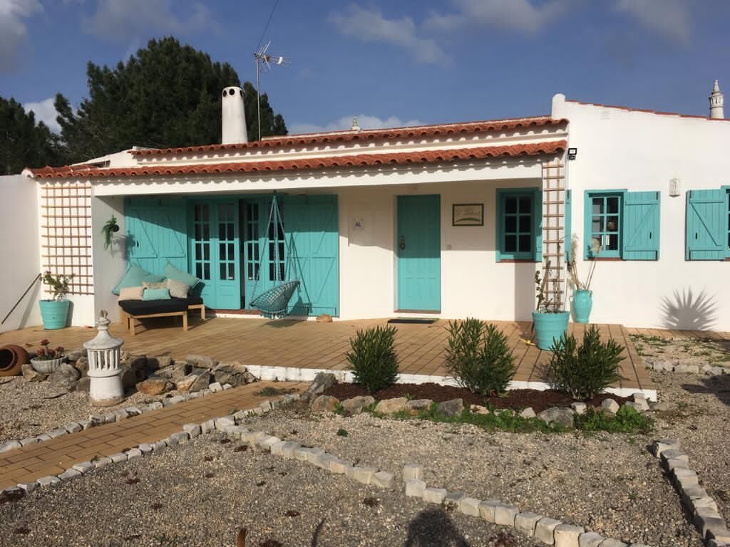A white building with turquoise shutters and a tiled roof.