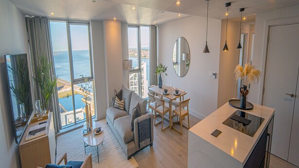 Een moderne woonkamer met een bank, salontafel en eethoek. Er is een groot raam met uitzicht op de zee.