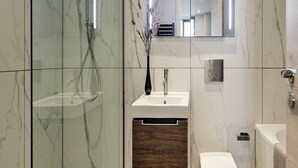 Een moderne badkamer met een douchecabine van glas, een houten wastafelmeubel, een witte wastafel en een toilet.