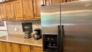 A kitchen with wooden cabinets, a stainless steel refrigerator, a coffee maker, and a small decorative house model.