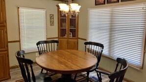 A dining room with a round wooden table, six chairs, a chandelier, and a cabinet with glass doors.