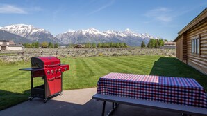 Un patio con una parrilla roja, una mesa a cuadros y vistas a la montaña.