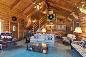 L’intérieur d’une cabane en rondins, avec un escalier, une cheminée, un canapé et une table basse.