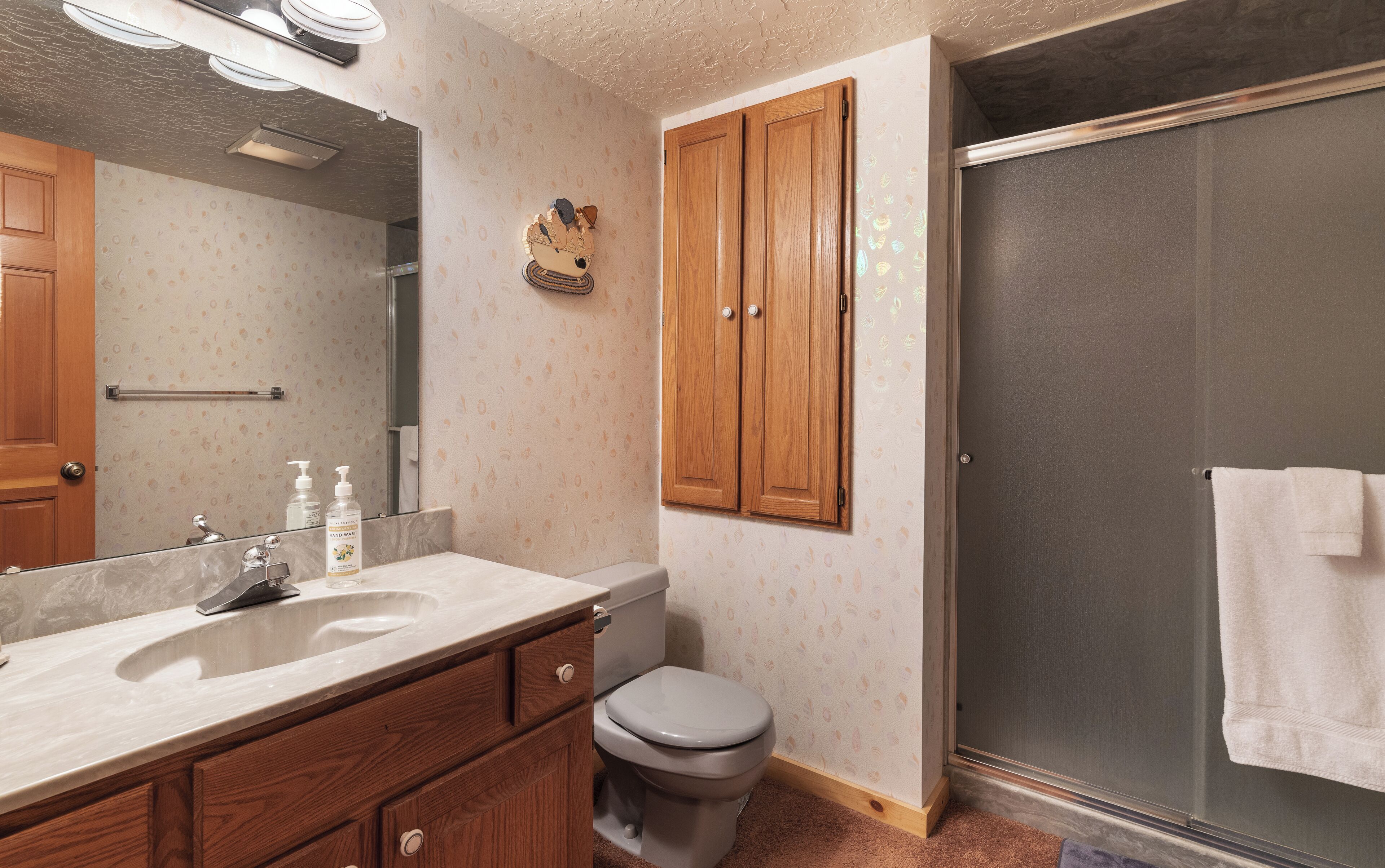 A bathroom with a wooden vanity, a toilet, a shower with a glass door, and a large mirror.