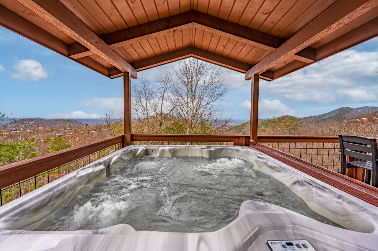 A hot tub under a wooden pergola with a view of a mountainous landscape.