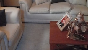 Un salon avec un canapé beige, un plaid à carreaux et une horloge au mur.