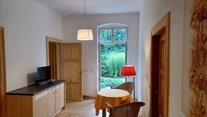A narrow hallway with wooden flooring, a dining table with a red lamp, and a television on a wooden cabinet. - Vacation apartment "Biene" in the listed Krahne art estate (Kloster Lehnin OT  Krahne)