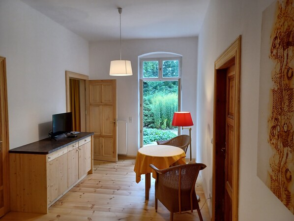 A narrow hallway with wooden flooring, a dining table with a red lamp, and a television on a wooden cabinet.