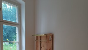 A room with a wooden cabinet with hooks, a wicker chair, and a door leading to a garden. - Vacation apartment "Biene" in the listed Krahne art estate (Kloster Lehnin OT  Krahne)