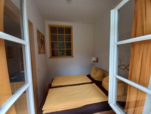 A narrow room with a bed, a window, and a wall-mounted light fixture.