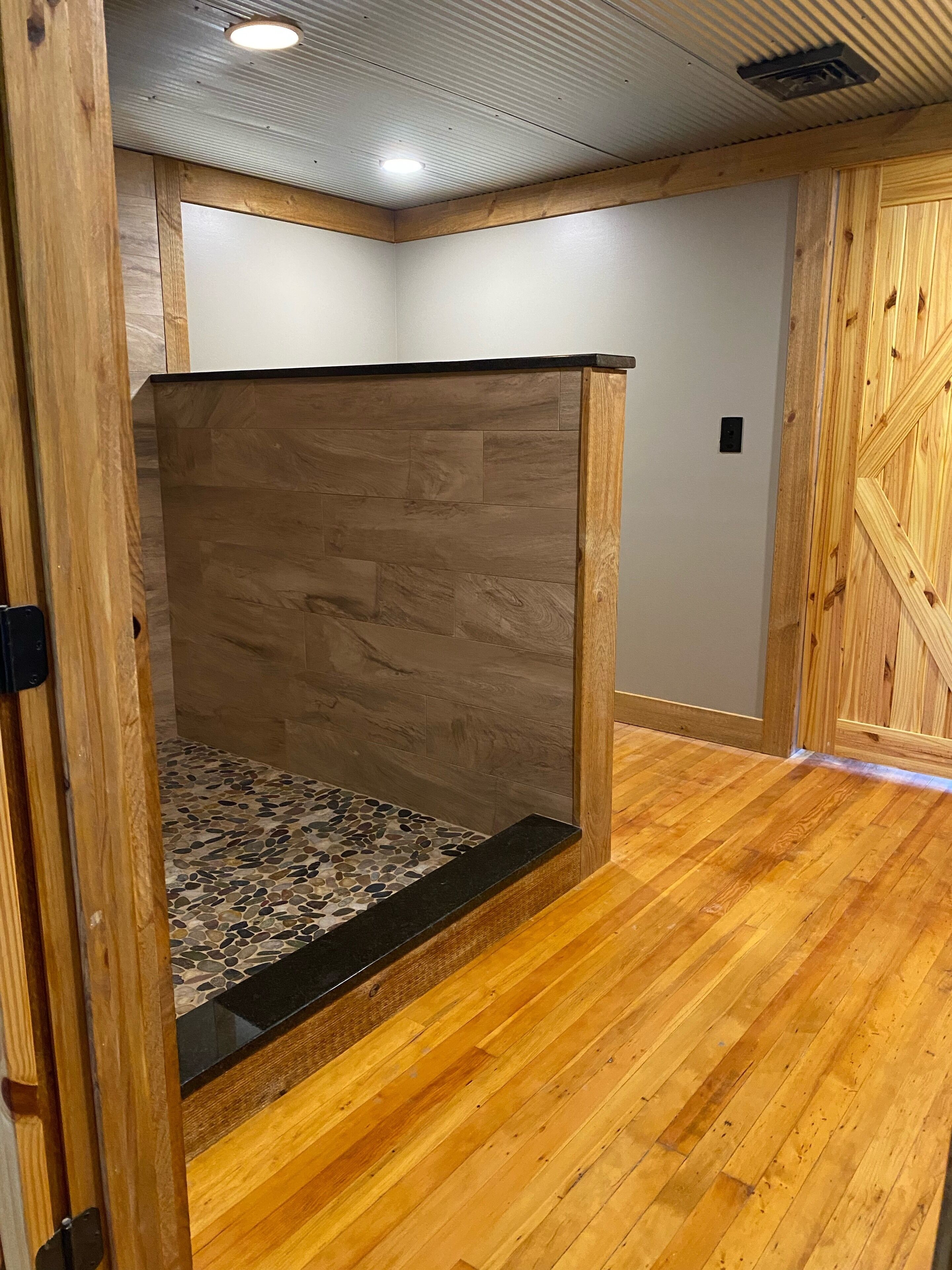 Une pièce dotée d’un plancher en bois, d’une zone de douche carrelée en pierre et d’une cloison en bois.