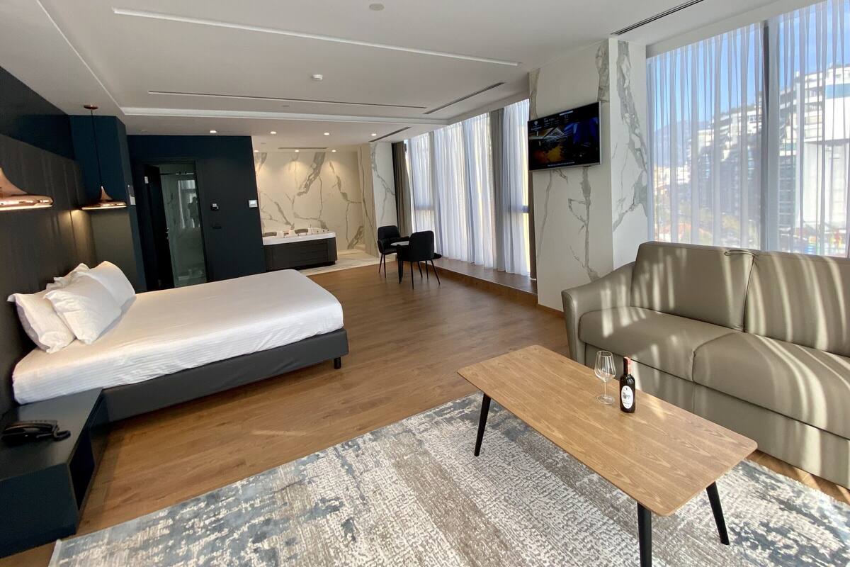 Une chambre d’hôtel moderne équipée d’un lit, d’un canapé, d’une table basse et d’un téléviseur fixé au mur.