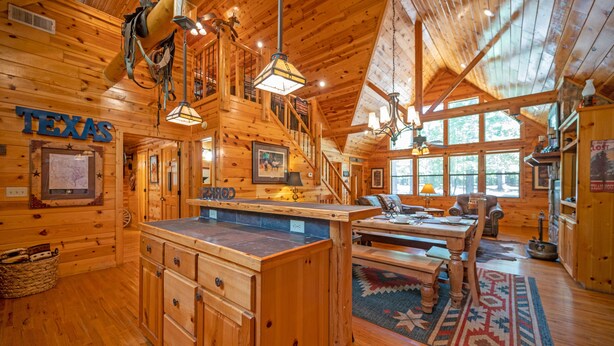 A log cabin interior with a wooden bar, dining area, and a staircase leading to an upper level. - TEXAS 2 STEP Luxury Log Cabin at the Entrance to Beavers Bend State park (Broken Bow)