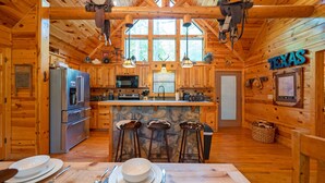 A wooden cabin interior with a kitchen, bar stools, and a Texas sign. - TEXAS 2 STEP Luxury Log Cabin at the Entrance to Beavers Bend State park (Broken Bow)