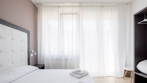 Una habitación de hotel moderna con una cama grande, una mesita de noche, un armario y cortinas de gasa.