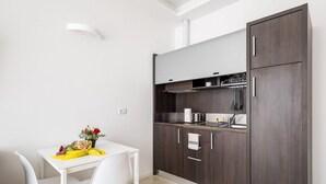 Una cocina compacta con armarios de madera oscura, una encimera blanca y un pequeño comedor con una mesa y sillas blancas.