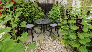 A garden patio with a round table and two chairs, surrounded by lush greenery and flowering plants. - Dreytop (Ryde)