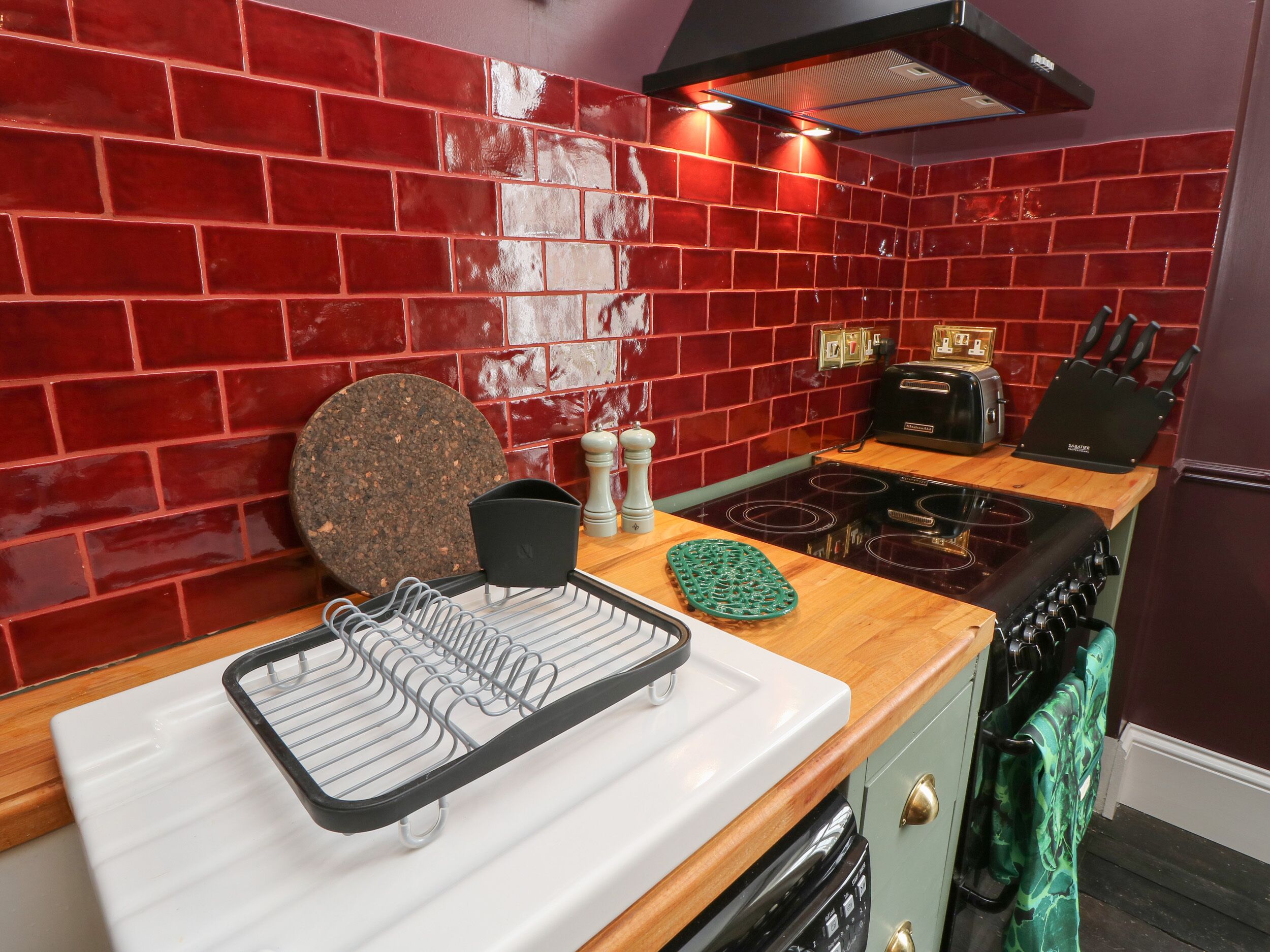 A kitchen with red brick walls, a black range hood, a toaster, a knife block, and a dish rack.