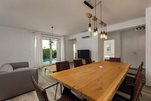 A modern living room with a large wooden dining table, wicker chairs, a grey sofa, and a TV. - Villa Aurora (Sveti Lovrec Labinski)