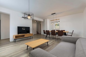 A modern living room with a sofa, a wooden coffee table, a TV, and a dining area with chairs and a table.