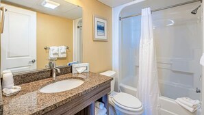 A bathroom with a granite countertop sink, a white toilet, and a glass-enclosed shower. - Ocean Views For Miles!! - Caravelle Resort #810 (Myrtle Beach)
