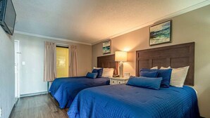 A hotel room with two beds, a nightstand, a lamp, a painting, and a door with curtains. - Ocean Views For Miles!! - Caravelle Resort #810 (Myrtle Beach)