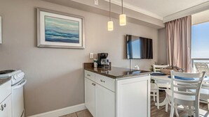 A compact kitchen with a dining area, a flat-screen TV, and a painting on the wall. - Ocean Views For Miles!! - Caravelle Resort #810 (Myrtle Beach)