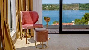 A room with a large window, a red chair, a small stool, and a decorative bowl on a table.