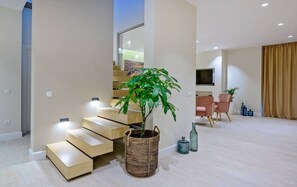 Uma sala de estar moderna com escada, uma grande planta em vaso, televisão de tela plana e área de jantar.