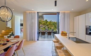 Una cocina moderna con comedor, vistas a zonas verdes y una escalera que sube a un nivel superior.