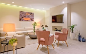 Una sala de estar moderna con un sofá, dos sillones rosas, una mesa de centro, un televisor y un cuadro en la pared.