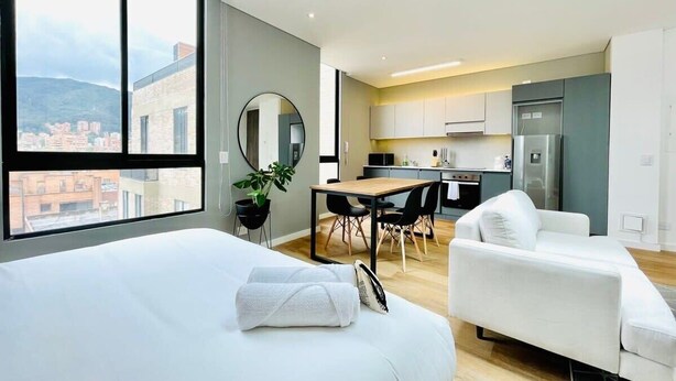 A modern hotel room with a large bed, a small sofa, a dining table, and a kitchen area. - w*| Modern Duplex in Parque Virrey (Bogotá)