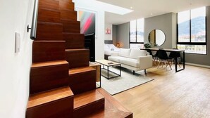 A modern interior with a wooden staircase leading to a living area, a dining table, and a sofa. - w*| Modern Duplex in Parque Virrey (Bogotá)