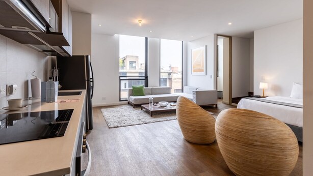Una camera d'albergo moderna con angolo cottura, un'ampia finestra vista città, un divano e un letto.