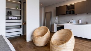 Una cucina moderna con mobili bianchi, forno integrato e microonde. Sono presenti sedie in vimini e uno scaffale bianco con asciugamani.