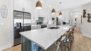 A modern kitchen with white cabinets, stainless steel appliances, a large island with bar stools, and pendant lighting. - Spacious Beachfront 3 Bedroom! (Destin)