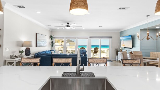 A modern kitchen with a large island, dining area with wicker chairs, and a view of the ocean. - Spacious Beachfront 3 Bedroom! (Destin)