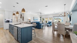 A spacious kitchen with a central island, a dining area with wicker chairs, and a living room with a blue sofa. - Spacious Beachfront 3 Bedroom! (Destin)