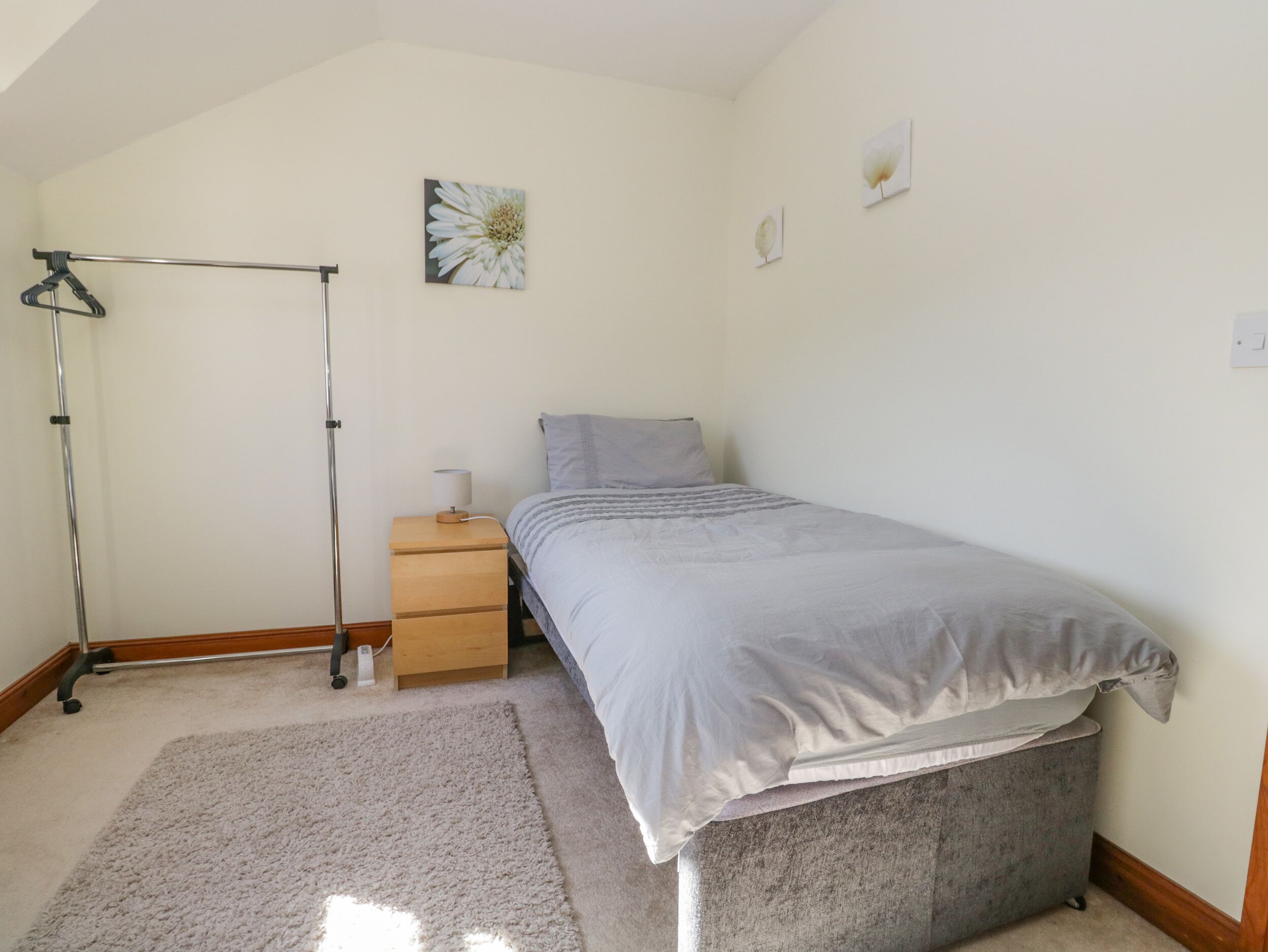 A bedroom with a bed, a nightstand, a lamp, a coat rack, and a picture on the wall.