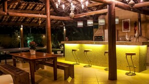 An outdoor patio with a wooden table, benches, and a bar area with stools. - Hotel Tetiaroa (Maraú)
