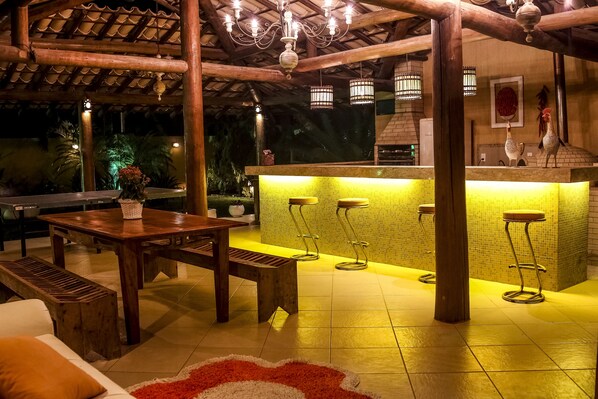 Un patio al aire libre con mesa de madera, bancos y zona de bar con taburetes.