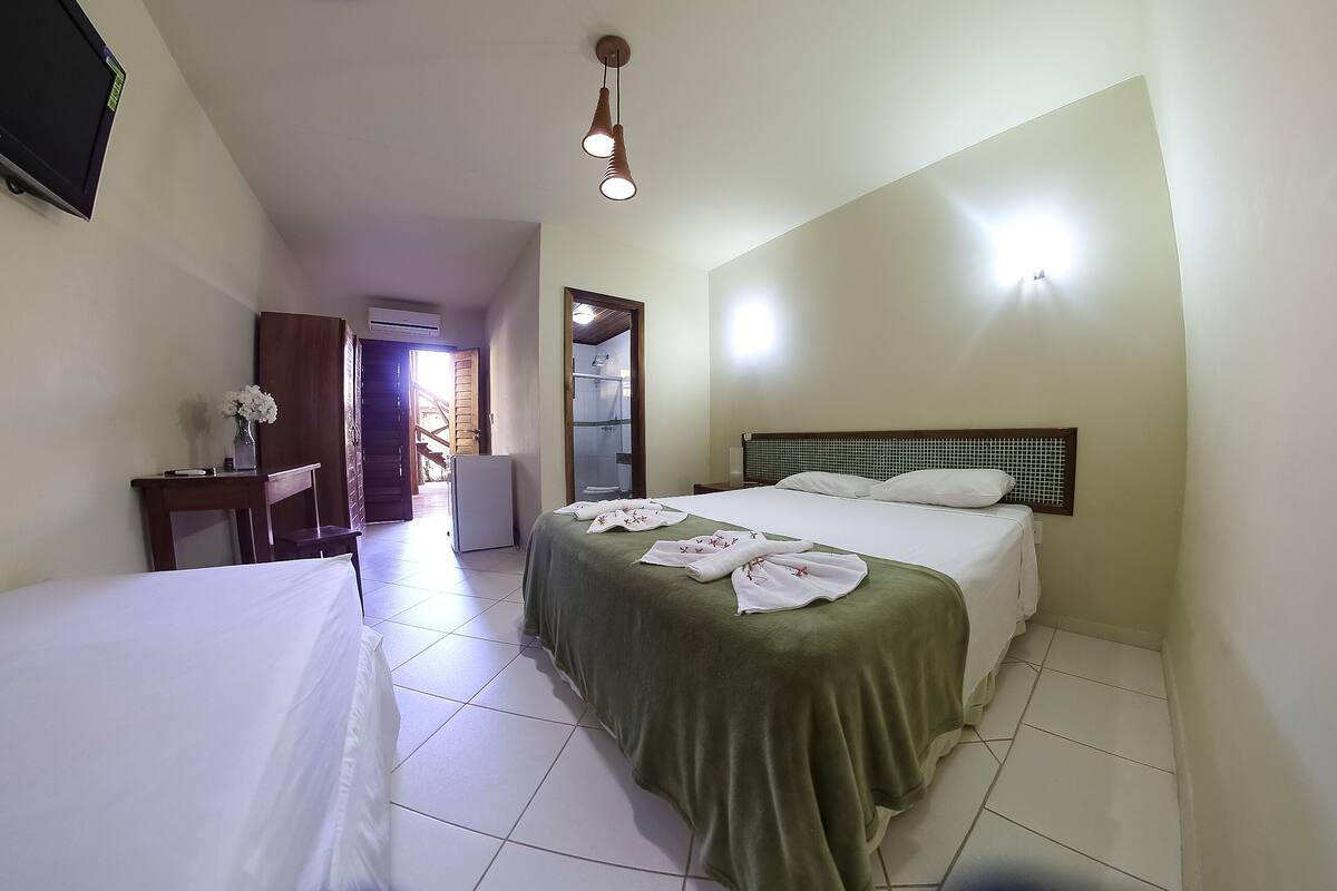 A hotel room with a bed, a desk, a chair, a TV, and a bathroom visible through an open door.