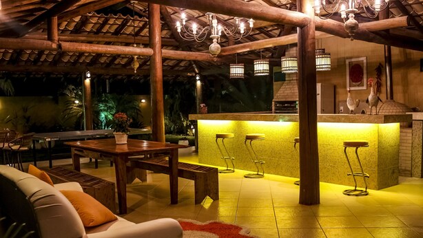 An outdoor patio with a wooden table and chairs, a bar area with stools, and a tiled floor. - Hotel Tetiaroa (Maraú)