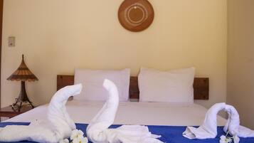 Quarto de hotel com cama, duas almofadas, uma luminária e duas toalhas moldadas em formato de cisnes sobre um cobre-leito azul.