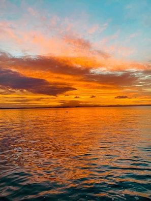 A sunset over a calm body of water with a distant shoreline. - Hotel Tetiaroa (Maraú)