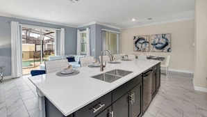 A modern kitchen with a large island, built-in appliances, and a sliding glass door leading to a patio. - Brand New Storey Lake Resort With Water Slides 4 Bedroom Townhouse by RedAwning (Kissimmee)