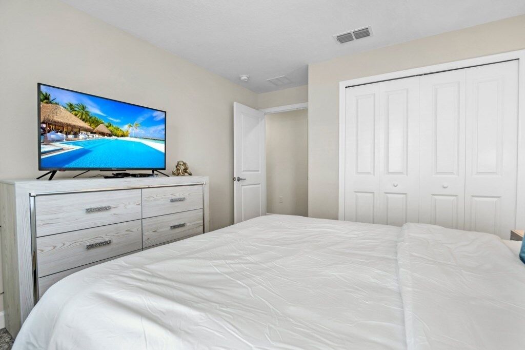 A bedroom with a large bed, a TV on a dresser, a wardrobe, and a door.