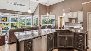 Una cocina moderna con armarios oscuros, una isla grande y una zona de comedor con un sofá marrón.