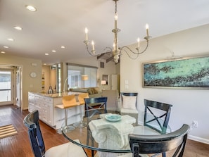 A modern kitchen with a dining area, featuring a glass table, dark chairs, and a chandelier. - 1581 Lagoon Villa ~ Beautiful Coastal Getaway in South Beach Marina Area! (Hilton Head Island)