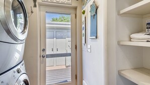 Zona de lavandería con una puerta que dice "BEACH HOUSE", una lavadora y un tendedero.